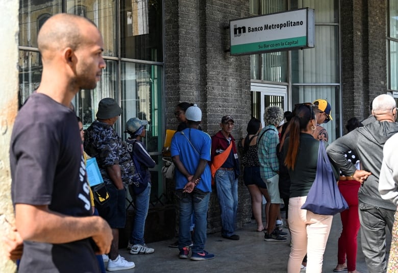 A line of people wait outside of a building under a sign for a bank