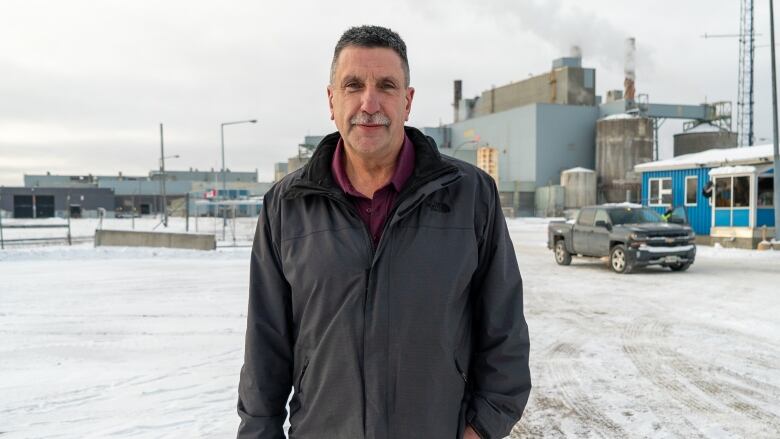 A man stands for a portrait in front of a factory. 