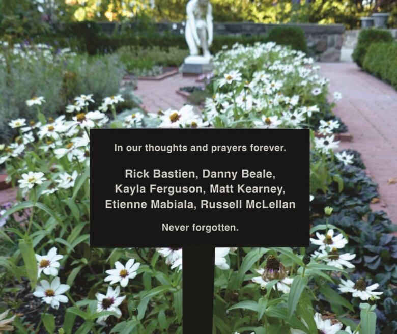 The names of six victims of an explosion on a plaque in front of a garden.