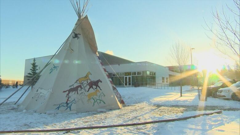 A tipi with horses painted on the side outside a large building