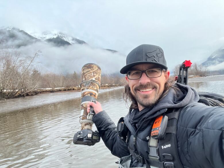 A man takes a selfie with a large camera in one hand