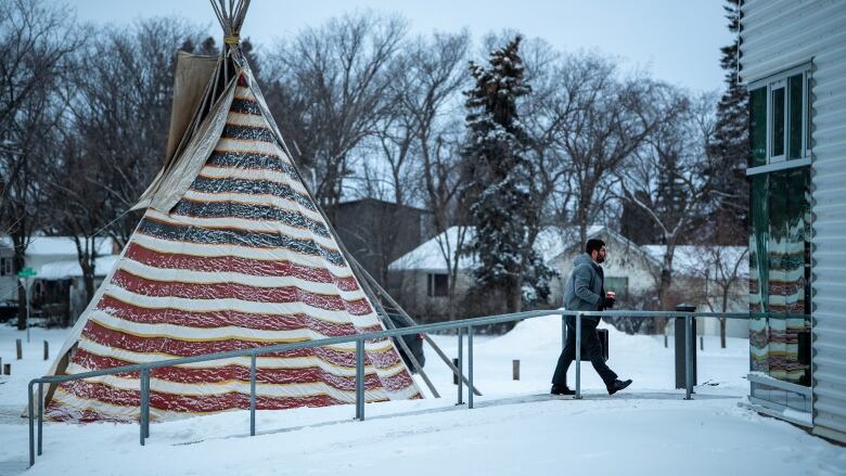 A man with a briefcase walks by a teepee on his way into a building.