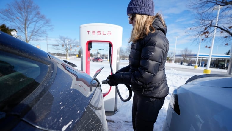 A person plugs in a black electric vehicle outside in winter.