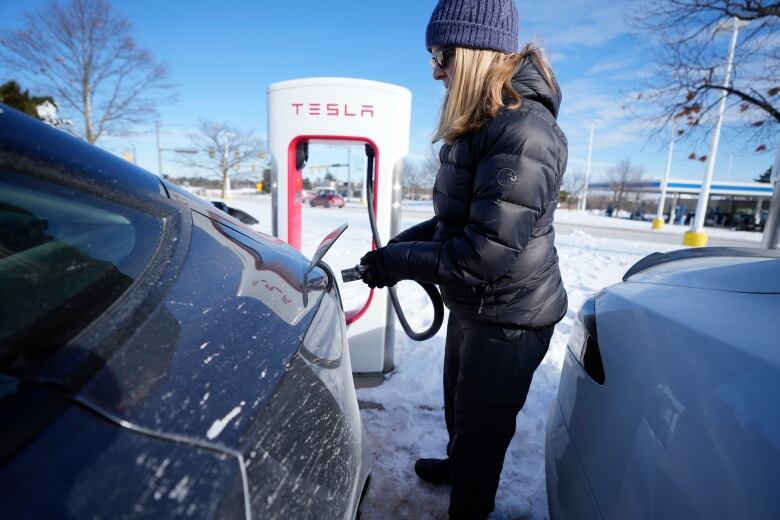 A person plugs in a black electric vehicle outside in winter.