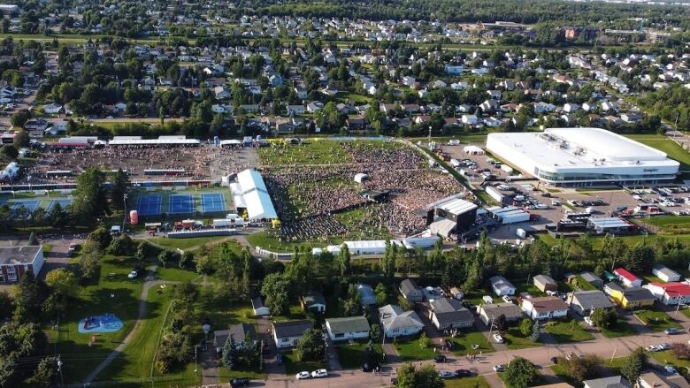 An aerial view of a field filled with a stage and people surrounded by homes.