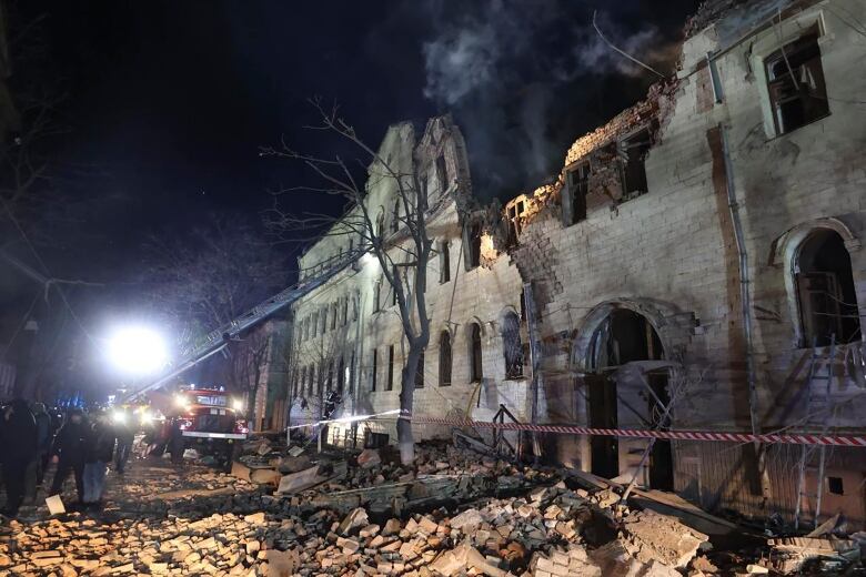 A fire truck ladder stretches to the top of a building that is partially collapsed after being hit by a rocket.