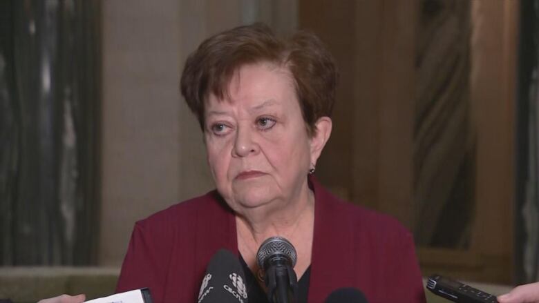 A woman stands in front of several microphones.