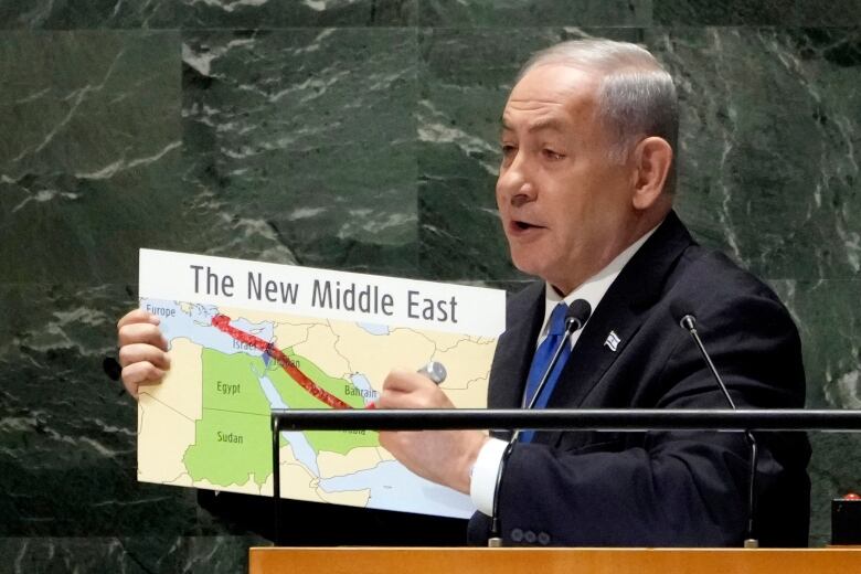 A man in a suit stands at a podium holding a map.