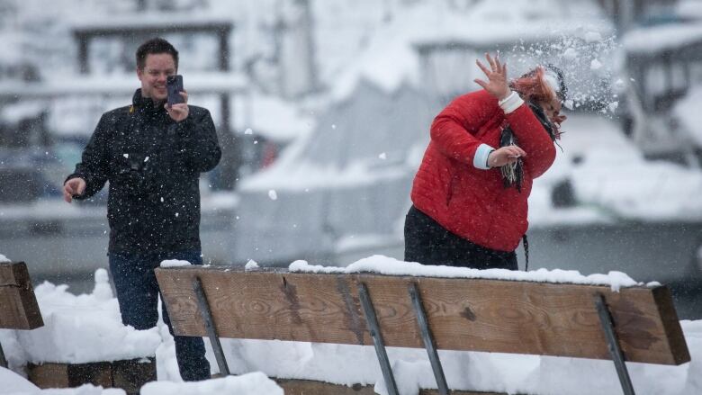 Two people throw snowballs at each other.