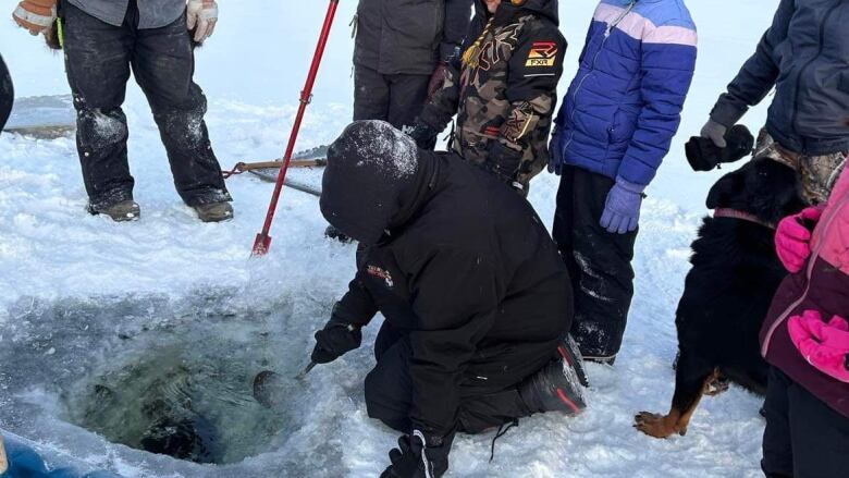 kids dressed in winter gear surround a hole in the ice