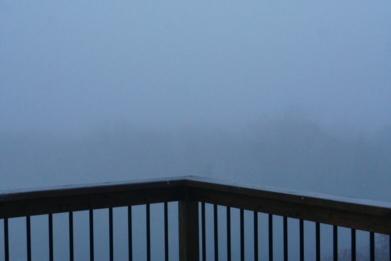 A deck railing and you can only see fog in the distance. 