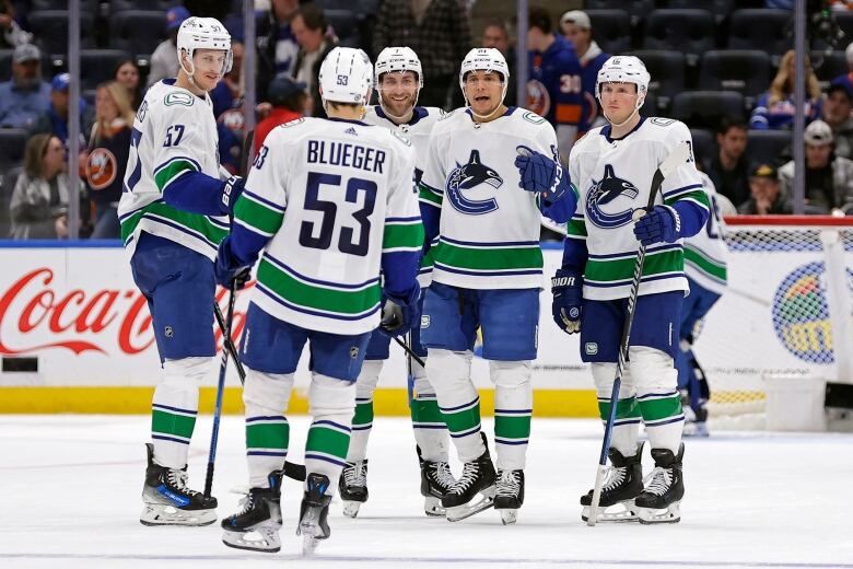 A group of hockey players, wearing white jerseys with green and blue trimmings, celebrate on the ice.