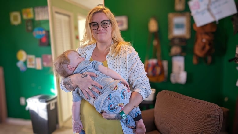 A woman holds a toddler in her arms, standing in a living room.