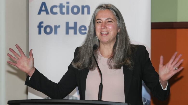 A woman stands at a podium with her arms outstretched.