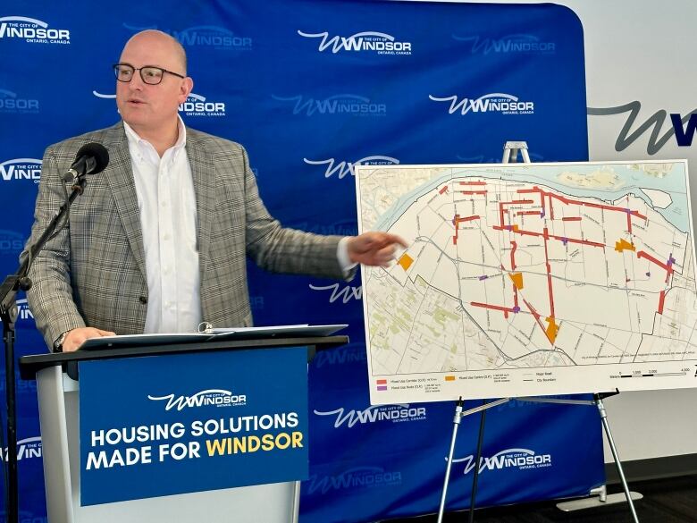 Dilkens standing at a podium with a map on an easel to his side. 