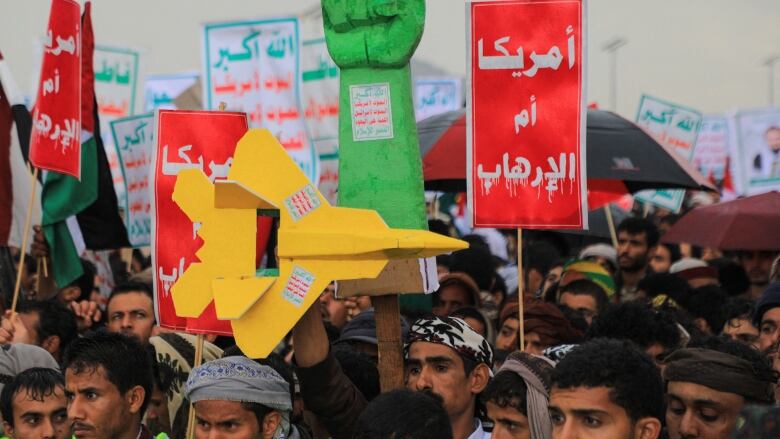 Protesters hold up signs in the shape of a fist and a fighter jet during a demonstration.