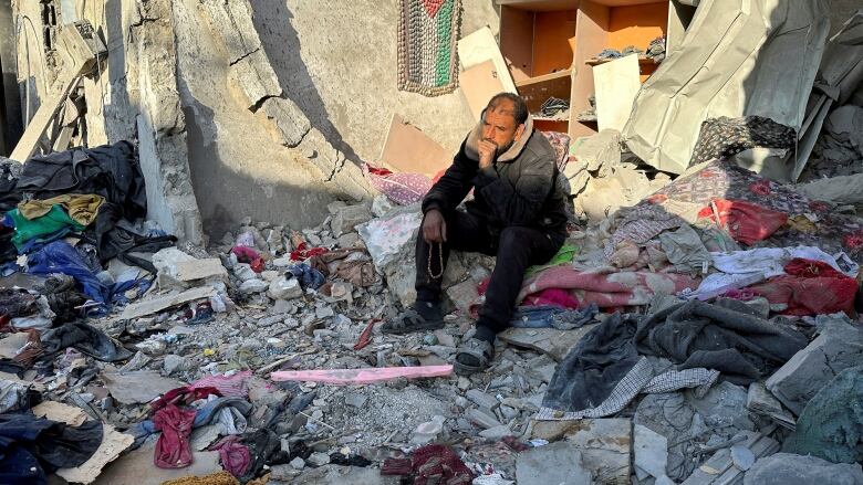 A man sits on rubble of a bombed-out building. 