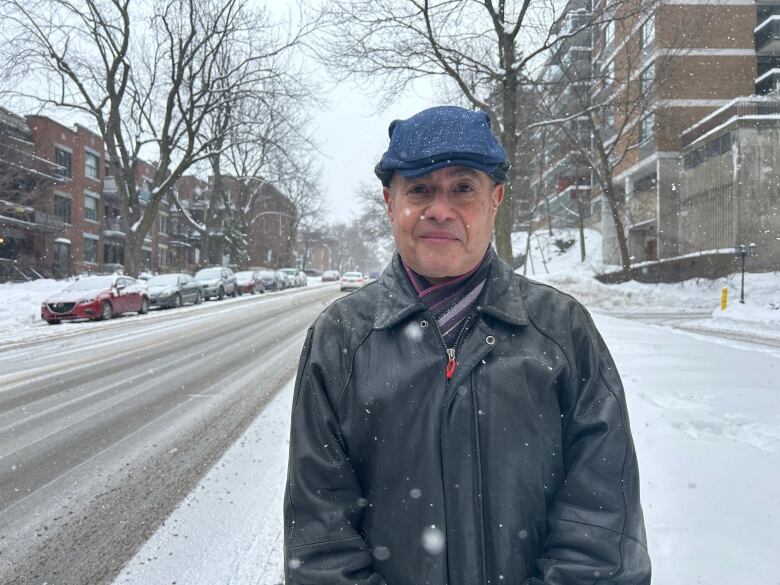 A man stands in the street under the falling snow.