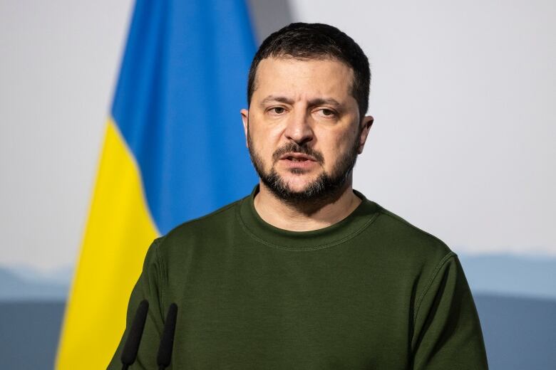 Ukrainian President Volodymyr Zelenskyy stands in front of a Ukrainian flag