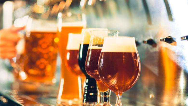 Several beer glasses lined up on a bar with different coloured beer in each glass.