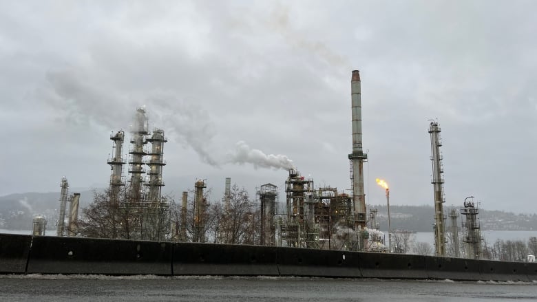 A large oil refinery spouts smoke amid a cloudy day.