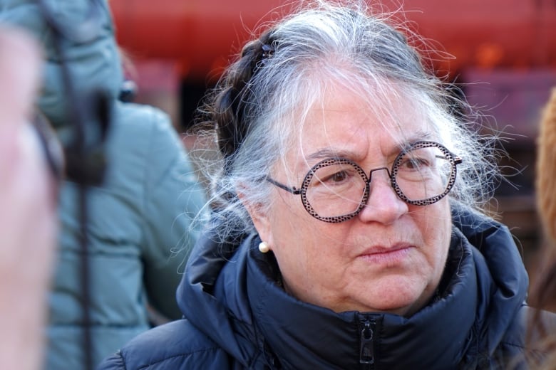 A woman looks concerned outside. She is wearing glasses and her hair is up in a bun.