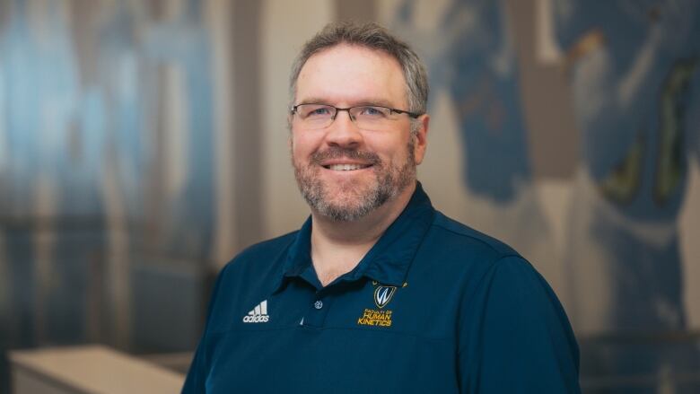 A man with greying brown hair wearing glasses and a dark blue polo shirt