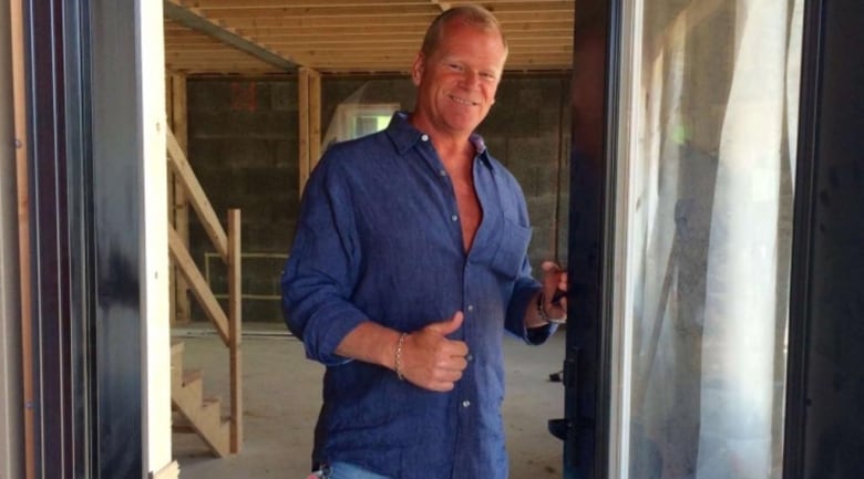 Mike Holmes giving a thumbs-up in the doorway at a house.