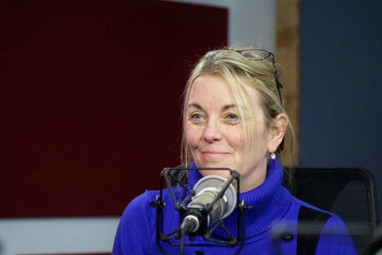 A woman with blonde hair and a blue sweater sitting behind a microphone. 