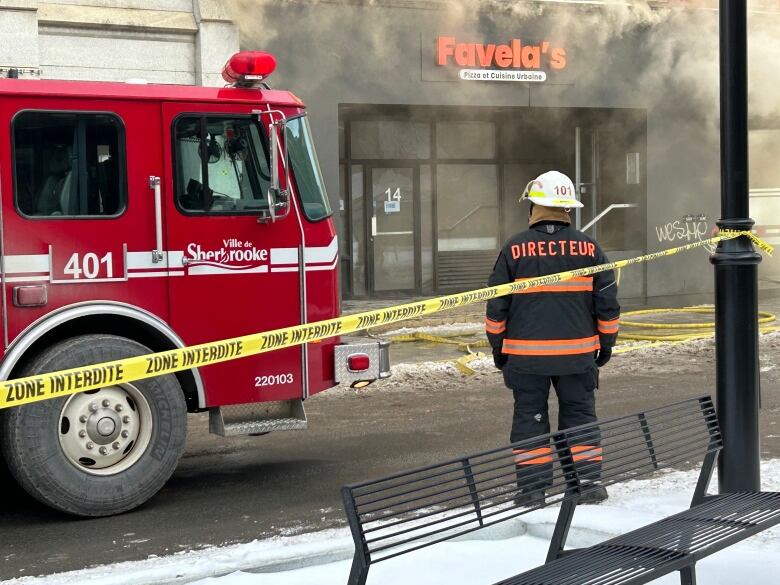 A firefighters stands with his back towards the camera looking at smoke coming from a building