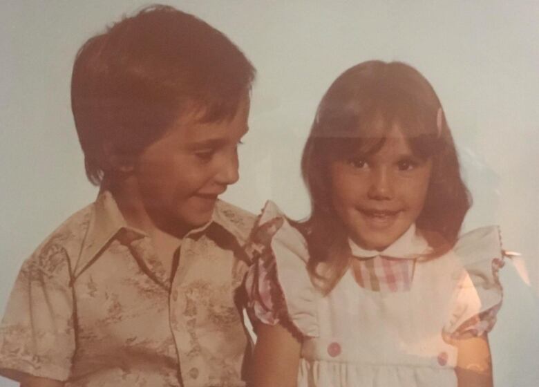 A film photograph of a young boy looking lovingly at his younger sister, who is smiling at the camera.