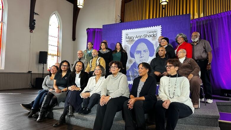 A group pf people sit posed in front of a large replica of a stamp