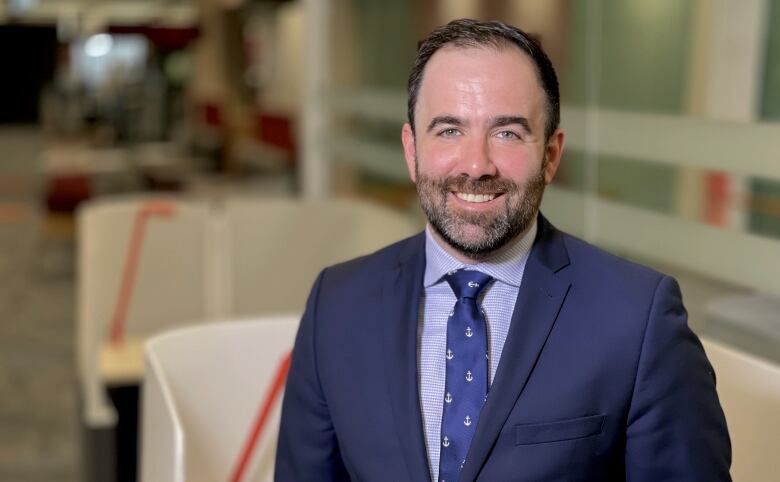 A bearded man in a navy blue suit poses for a portrait.