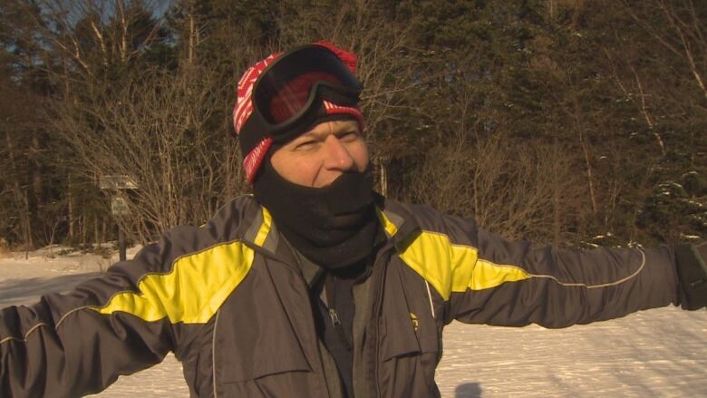 Man standing outdoors in winter jacket, with arms spread out.