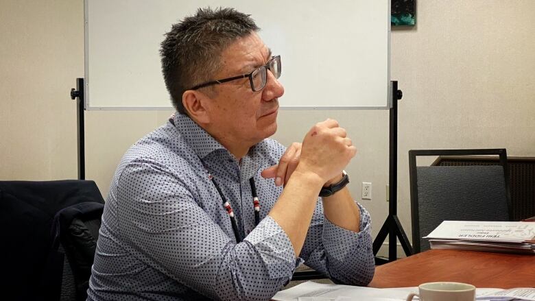 A man with glasses rests his elbows on a table. 