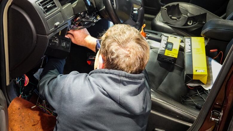 A technician installs a security system under a vehicle's steering wheel.