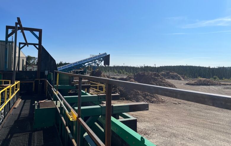 a lumber mill equipment sits in a lumber yard surrounded by piles of sawdust.