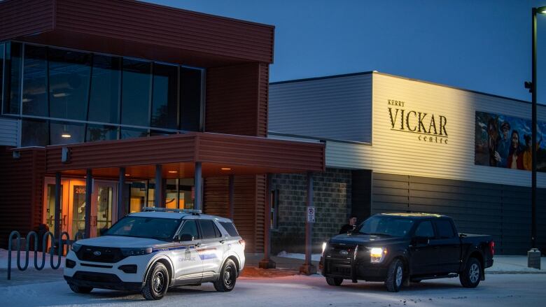 A police SUV and a truck sit outside a building on a dark day.