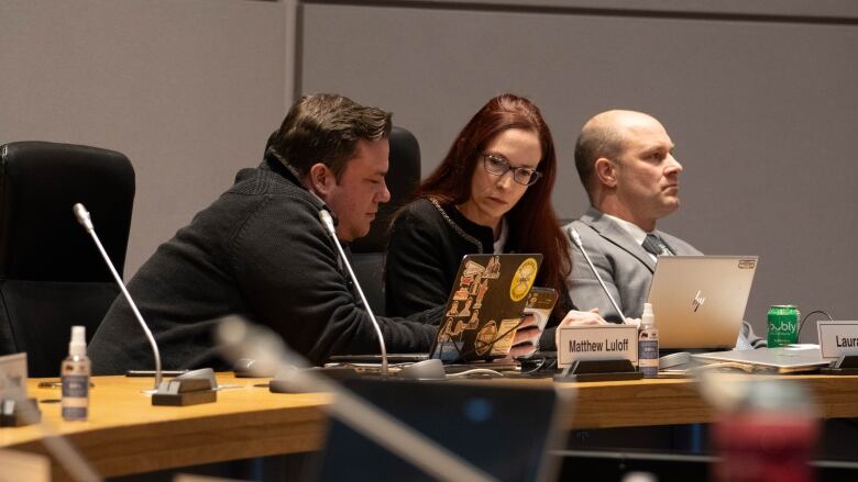 A man in a black sweater leans toward a red-haired woman who reads something on the cell phone in his hand.