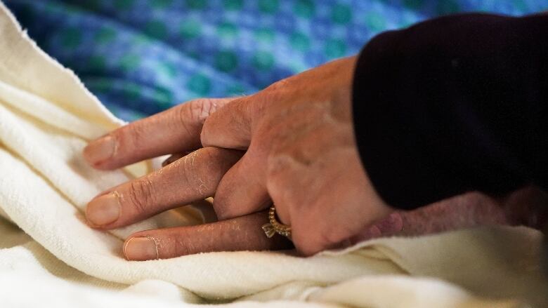 Close-up photo of one person holding the hand of another person, in what appears to be a bed.