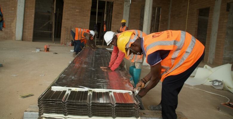 Construction workers in hard hats and safety vests crouch over a tray of metal beams