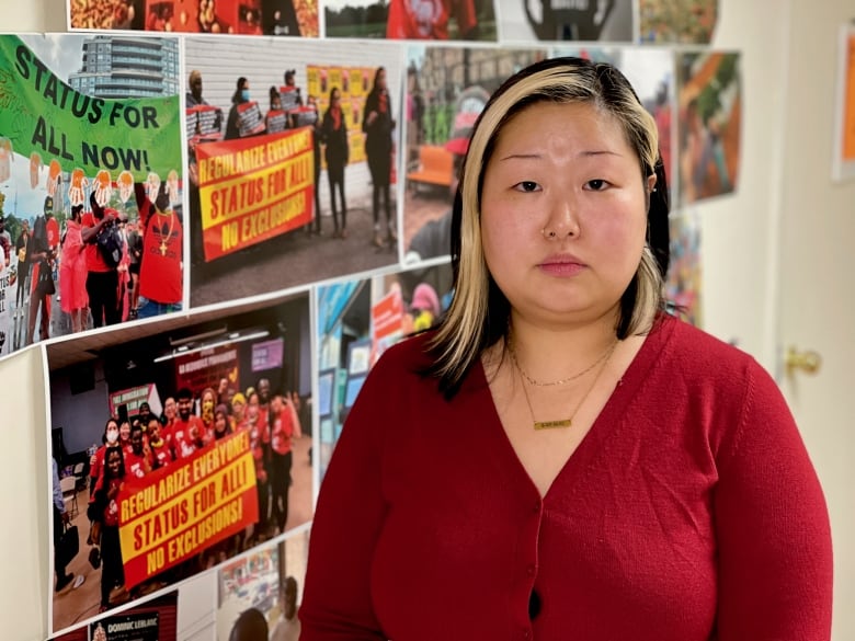 A woman in a red sweater stands before a colourful wall of photos depicting past protests.