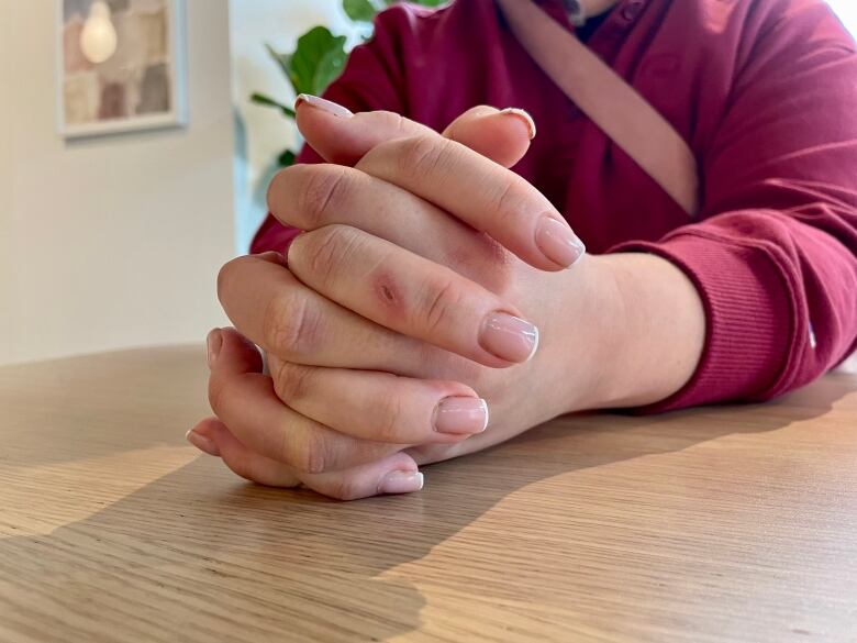 Hands folded together resting on a light wood table, subject wearing a red sweatshirt.