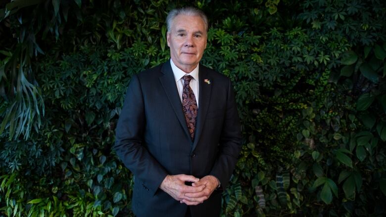 A white man wearing a patterned tie poses in front of a plant wall.