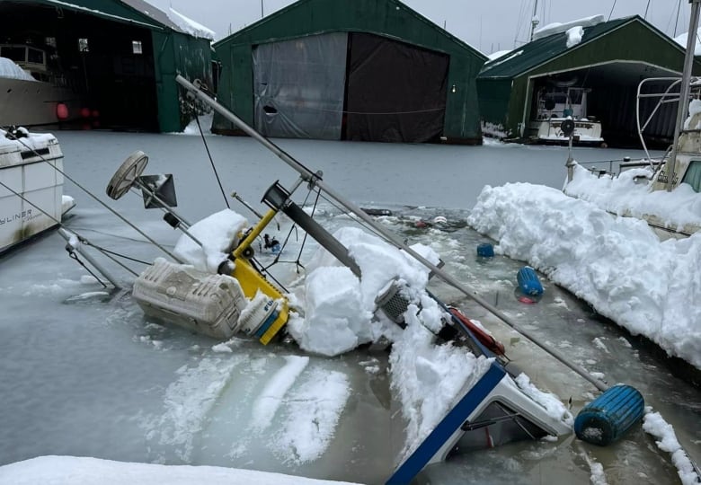 Boats tipped over in the water and covered in snow.