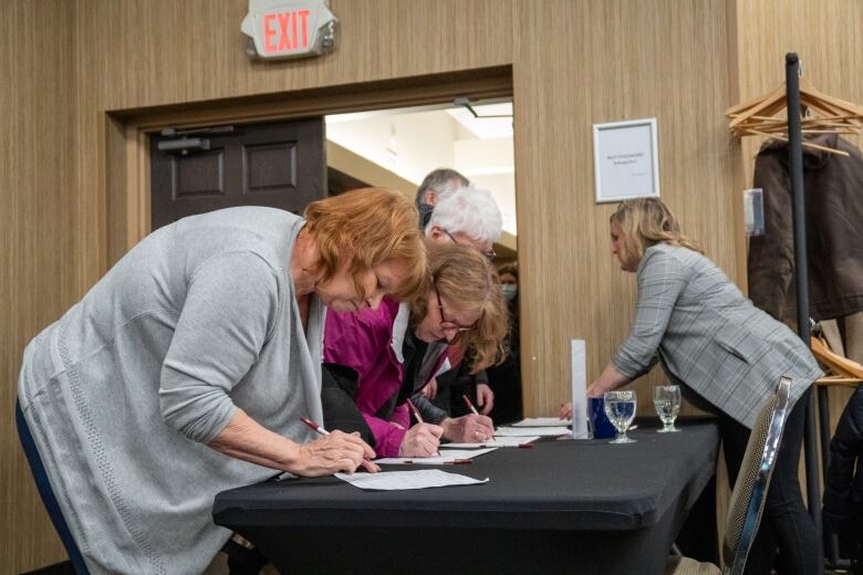 People hunch over a table and sign their names. 