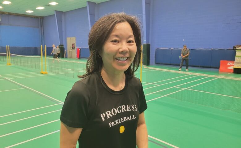 A woman in a black t-shirt stands on a pickleball court.