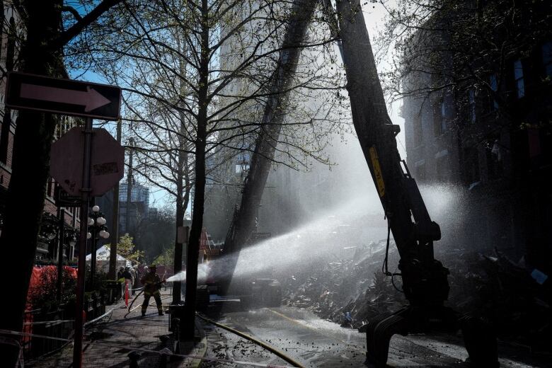 A firefighter sprays water on debris during demolition of the Winters Hotel in Vancouver, B.C., Friday, April 22, 2022.