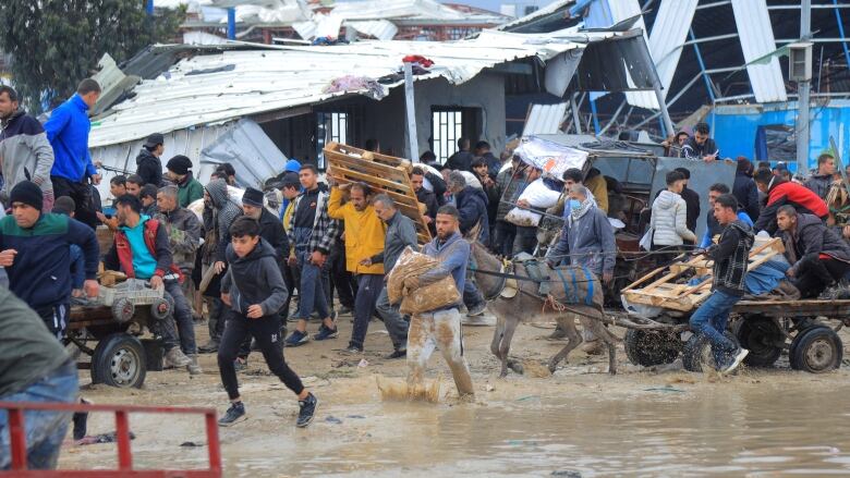 A crowd of people carries items through mud. 