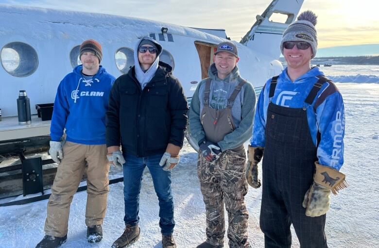 Four men stand in front of an aircraft turned into an ice fishing shack.